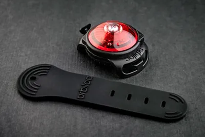 A red and black safety light and its black strap are placed on a dark gray surface.
