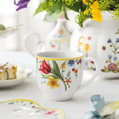 A close-up of a floral patterned mug with a slice of cake and other tableware in the background.
