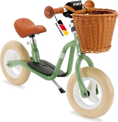 A green Puky balance bike with a wicker basket and brown seat and handlebars, shown against a white background.