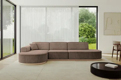 A modern living room with a large sectional sofa, large windows with sheer curtains, and a coffee table.