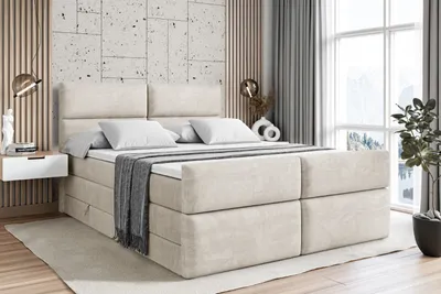 A bedroom scene with a large bed as the focal point, decorated with pillows and a throw blanket. The room has a modern, minimalist aesthetic with textured walls and large windows.