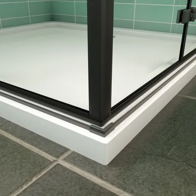A close-up view of the corner of a modern shower enclosure, showing the black frame, glass door, and white shower tray, set against green tiled walls and dark tiled flooring.