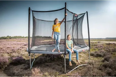 Two girls on a trampoline in a natural outdoor setting.