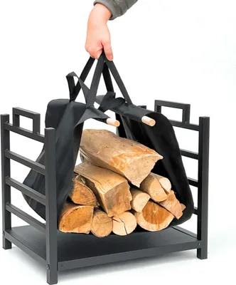 A hand holding a firewood carrier filled with logs, placed inside a metal firewood rack.