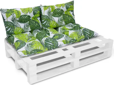 A white wooden pallet sofa with green and white leaf-patterned cushions.