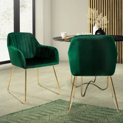 Two green velvet dining chairs with gold legs are placed around a dark marble-topped dining table in a well-lit room.