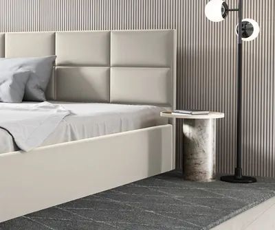 A close-up view of a bed with a beige upholstered headboard and a bedside table with a lamp.