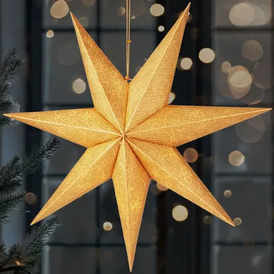 A golden star-shaped Christmas decoration hangs in front of a window with bokeh lights.