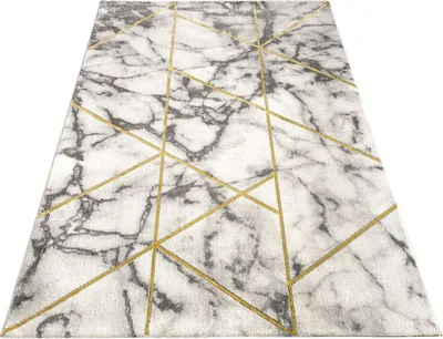 A close-up, angled view of a rug with a marble pattern and geometric gold lines.