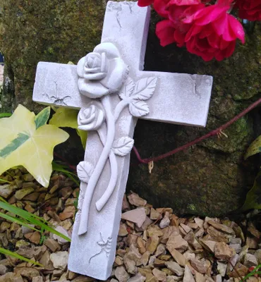A stone cross with a rose design, placed outdoors among rocks and foliage.
