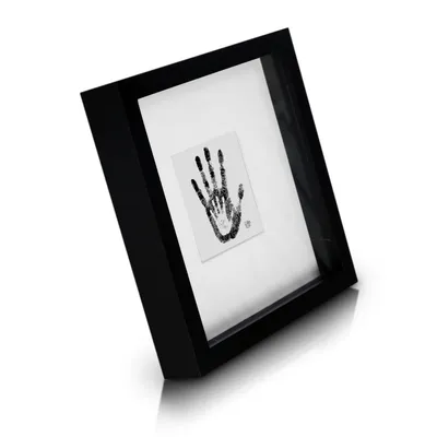 A black shadow box picture frame with a white mat and a black handprint on it, shown at an angle on a white background.