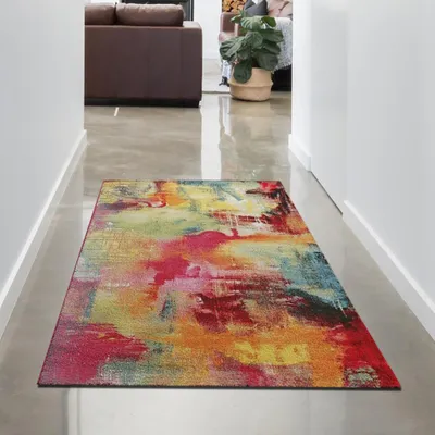 A colorful abstract rug is placed on a polished concrete floor in a hallway, with a living room visible in the background.