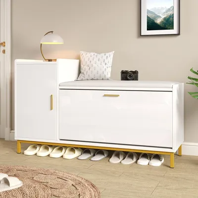 A white shoe cabinet with a padded seat and gold metal legs, with shoes stored underneath.