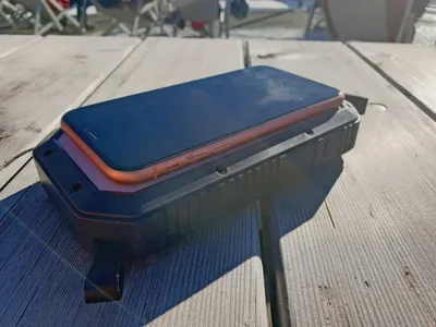 A smartphone is charging on a power bank on a wooden table outdoors.