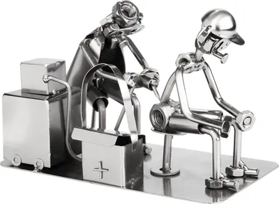 A metal sculpture of two figures, one appearing to be a tattoo artist working on another figure, with a toolbox and equipment nearby.
