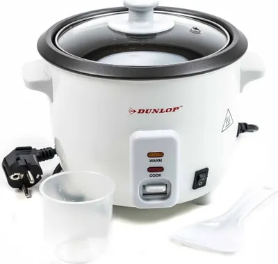 A white electric rice cooker with a glass lid, control panel, power cord, measuring cup, and rice paddle, set against a white background.
