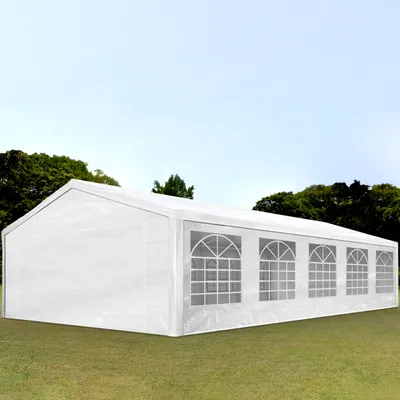 A white party tent with arched windows is set up on a grassy lawn with trees in the background.