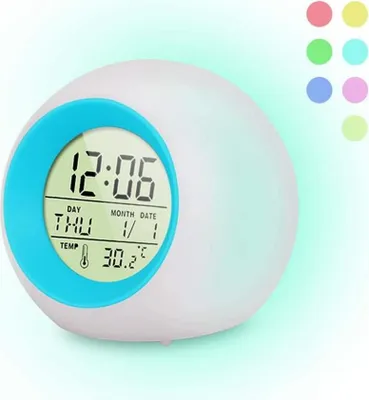 A digital alarm clock with a blue rim and a digital display showing the time, day, month, date, and temperature. The clock is illuminated with a soft glow.