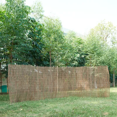 A woven reed fence is set up in a grassy area with trees in the background.