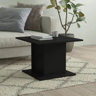 A black coffee table is placed on a rug in a living room setting, with a sofa and a plant in the background.
