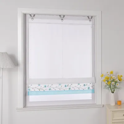 A window with a roman blind decorated with a floral pattern and a blue stripe, next to a vase of yellow flowers on a nightstand.