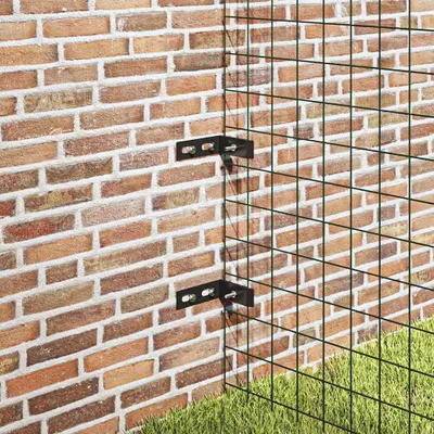 Corner brackets attaching a green wire mesh fence to a brick wall, with grass in the foreground.