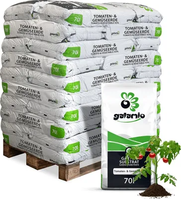 A stack of soil bags on a pallet, with a single bag and a tomato plant in the foreground.