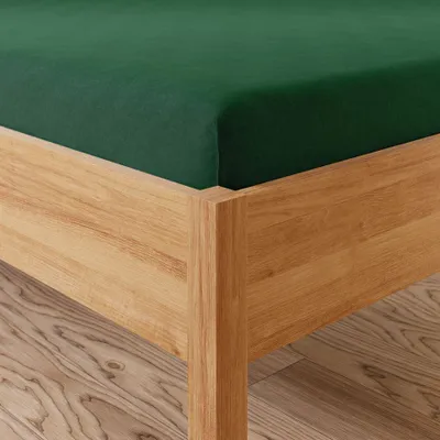 A close-up view of a dark green fitted sheet on a wooden bed frame.