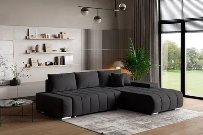 A modern living room with a dark gray sectional sofa, a coffee table, shelves with decor, and a large window overlooking a garden.