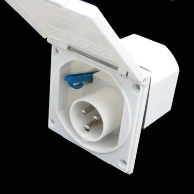 A close-up, angled view of a white CEE outdoor socket with its protective cover open, revealing the three-pin connector inside. The background is black.