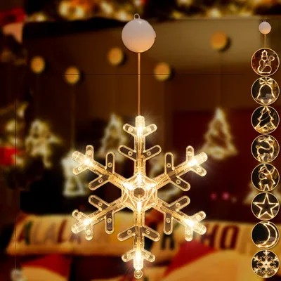 A snowflake-shaped LED light decoration hangs in a dimly lit room, with other Christmas-themed lights and decorations visible in the blurred background.