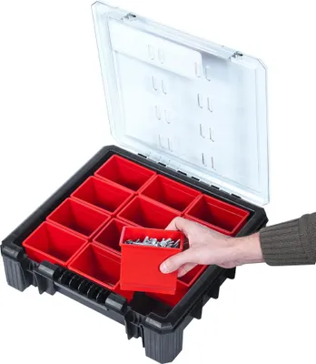 A hand is shown placing a small red bin filled with screws into a larger black organizer box with multiple red bins and a clear lid.