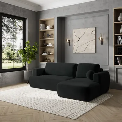 A modern living room with a black sectional sofa, bookshelves, and a large window.