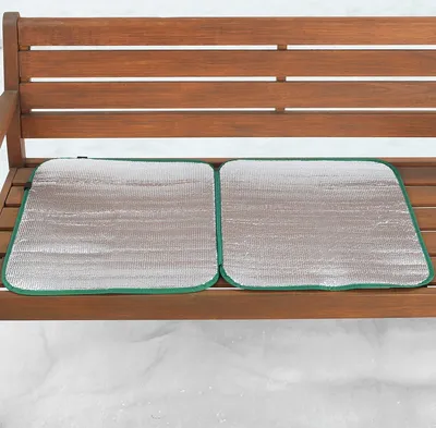 Two silver seat cushions with green trim are placed on a wooden bench in a snowy environment.