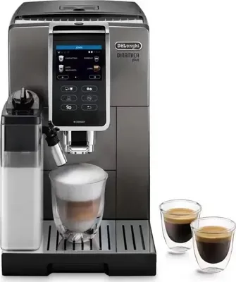 A De Longhi Dinamica Plus automatic coffee machine is shown with a glass of coffee with foam, a milk container, and two small espresso cups.