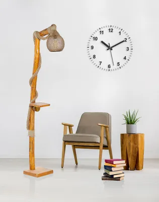 A floor lamp with a wooden base and a rope-wrapped pole, next to a chair and a stack of books.