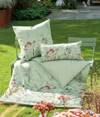 Bedding set with pillows and a duvet laid out on a green garden chair in a garden setting.