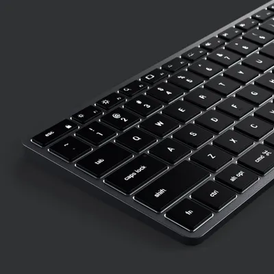 A close-up, angled view of a black wireless keyboard with illuminated white keys against a dark gray background.