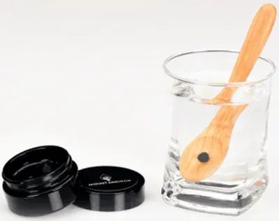 A wooden spoon in a glass of water next to an open container of Shilajit.
