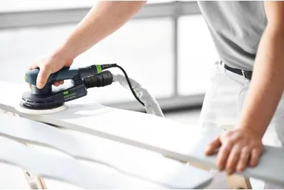 A person is using a Festool sander on a white wooden surface.
