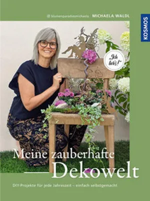 A woman is kneeling next to a wooden chair decorated with plants and a fairy figurine. The book cover is for "Meine zauberhafte Dekowelt".