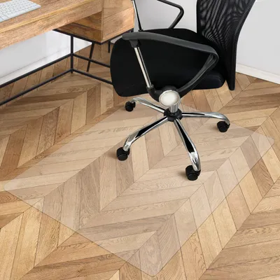 An office chair mat on a wooden floor next to a desk.
