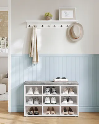 A shoe bench with storage compartments and a shelf with hooks above it, in a hallway or entryway.