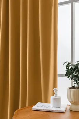 A close-up view of a mustard yellow curtain hanging next to a window, with a small plant and decorative item on a table in the foreground.