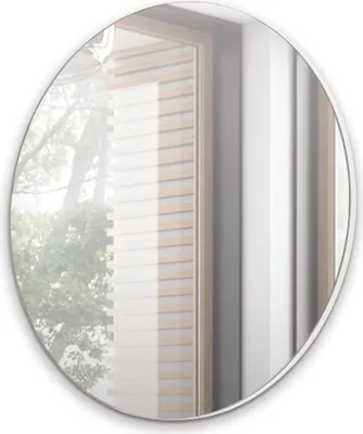 A round mirror reflecting a window with wooden blinds and trees outside.