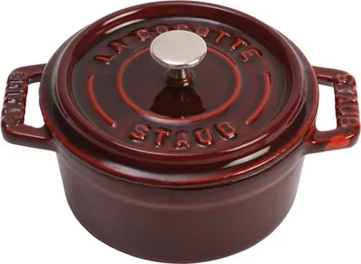 A close-up studio shot of a small, dark red Staub cocotte pot with a silver knob on the lid.