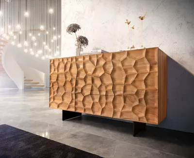 A wooden sideboard with a 3D textured front is displayed in a modern, well-lit interior with a staircase and chandelier in the background.