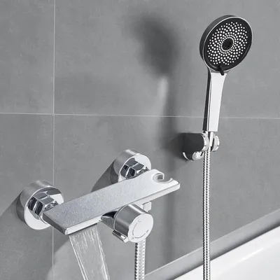 A modern bathroom faucet with a waterfall spout and a handheld showerhead mounted on a tiled wall.