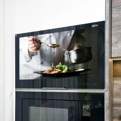 A chef is shown on a screen in a kitchen, preparing food.