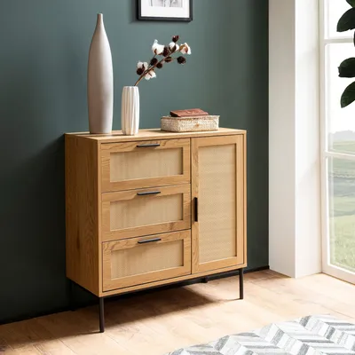 A modern wooden sideboard with rattan accents is shown in a room with a teal wall and a window.